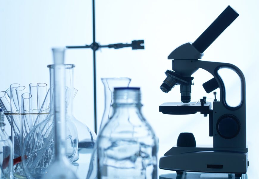 Laboratory bench with modern microscope, test tubes, glass bottles and flasks, white background